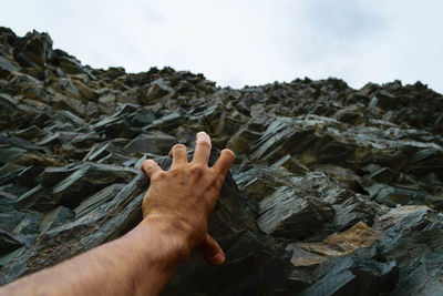 Cropped hand of man holding rock against sky