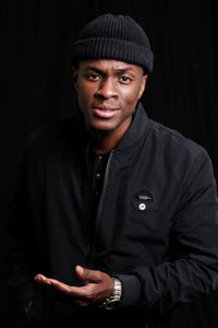 Portrait of young man standing against black background