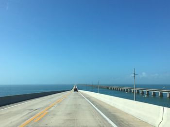 Road by sea against clear blue sky