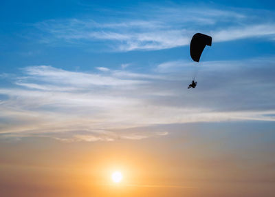 Low angle view of people paragliding against sky during sunset