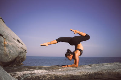 Woman practicing yoga at beach against sky