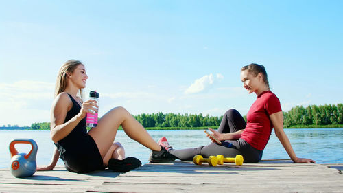 Two beautiful, athletic blonde girls, women have rest after training outdoors, drink water, talk