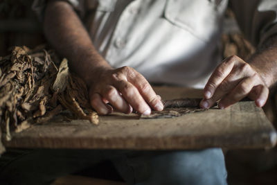 Midsection of man rolling dry leaves on table at workshop