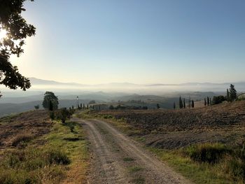 Dirt road amidst field against clear sky