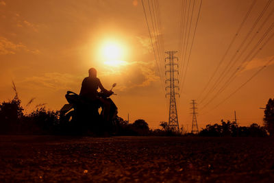 Silhouette people on electricity pylon against sky during sunset