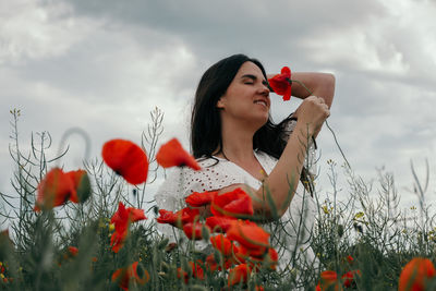 Portrait of beautiful young woman wearing white dress, standing in poppy field