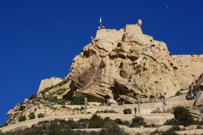 Low angle view of castle on mountain against blue sky