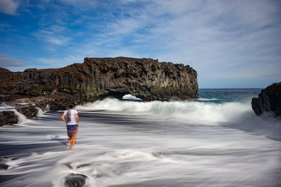 Rear view of man standing on rock by sea against sky