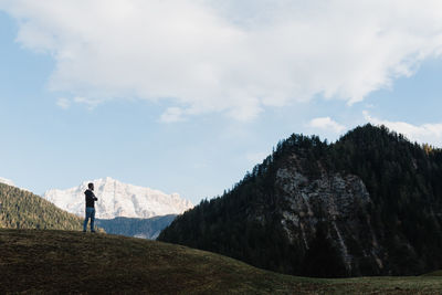 Man standing on hill amidst mountains against sky