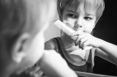 Reflection of boy holding comb on mirror in bathroom