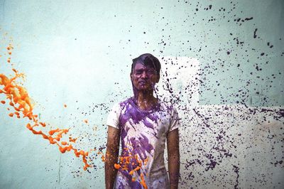 Man standing amidst splashing paints against wall