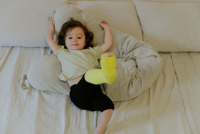 A baby girl with a cast on her leg lies on the bed.