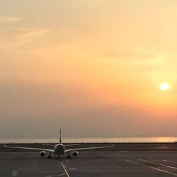 Airplane on airport runway against sky during sunset