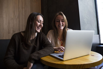 Two happy friends sitting in a coffee shop looking at laptop