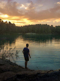 Man standing on lake against sky during sunset