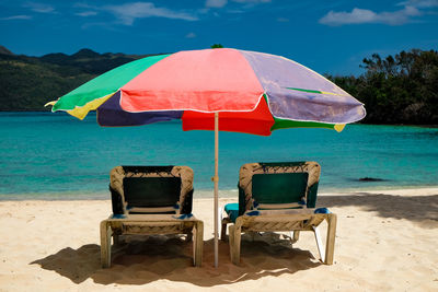 Deck chairs on beach against sky