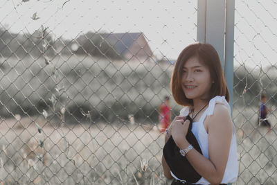 Portrait of smiling young woman standing by fence