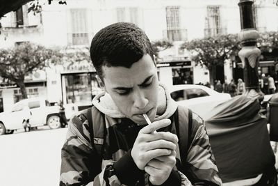 Young man lighting cigarette while sitting in city
