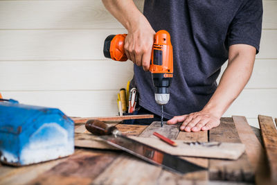 Midsection of carpenter drilling wood