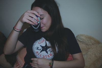 Young woman holding beer can against face at home