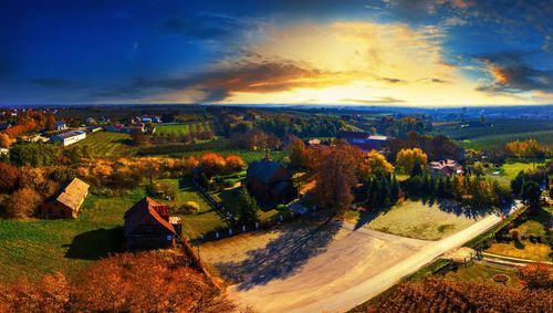 Scenic view of field by houses against sky during sunset