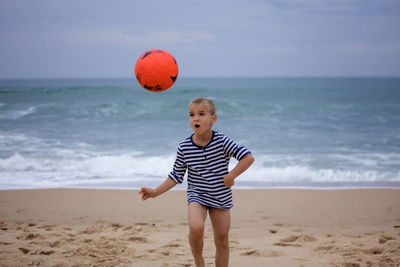 Full length of boy playing soccer at beach