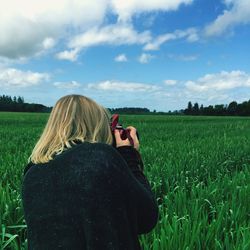 Rear view of woman photographing on field against sky