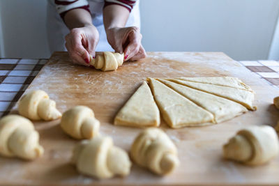 Woman making croissants from sliced dough on cutting board in kitchen