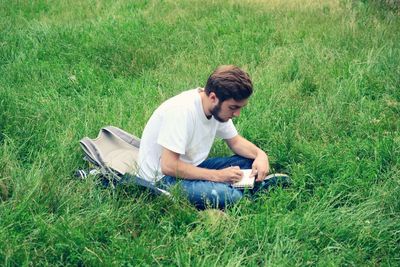High angle view of man writing in book while sitting on grass at park