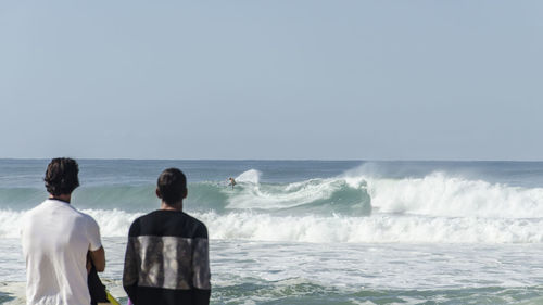 Rear view of men looking at surfer against clear sky