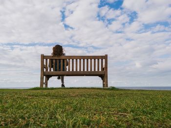 Rear view of woman sitting on bench against sky