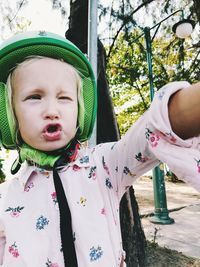 Cute girl winking while wearing green helmet against trees