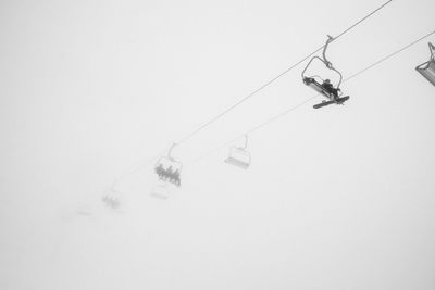 Low angle view of ski lifts against sky during foggy weather