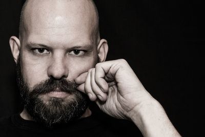 Portrait of man touching mustache against black background