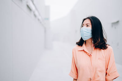 Young woman looking away while standing against wall