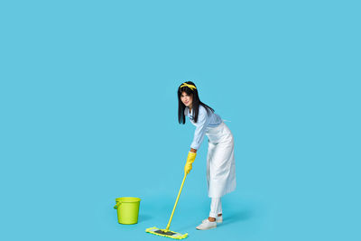 Low angle view of young woman holding umbrella against blue background