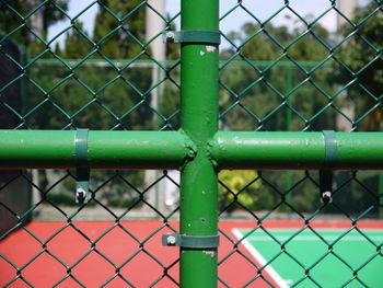 Close-up of plus shape pipe on chainlink fence against tennis court