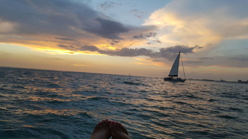 Low section of man on sea against sky during sunset