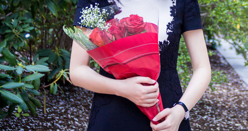 Midsection of woman holding red while standing outdoors