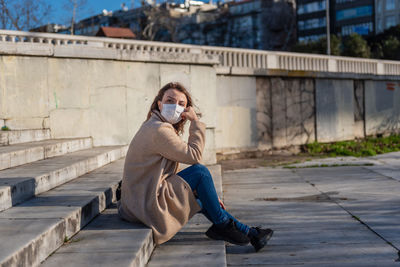 Full length of young woman using mobile phone while sitting on bridge