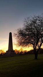 Silhouette trees on field against clear sky at sunset