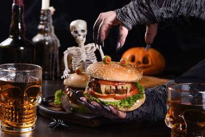 The witches hands hold a monster burger in her palms on a sitting skeleton.halloween party appetizer