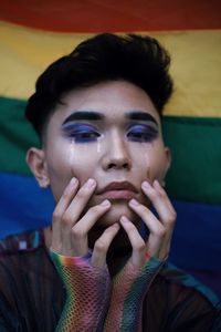 Portrait of young man with make-up against rainbow flag