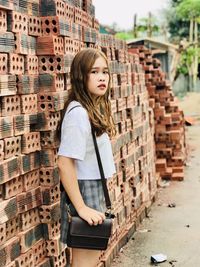 Portrait of beautiful young woman standing against bricks