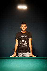 Portrait of young man standing against illuminated wall at night