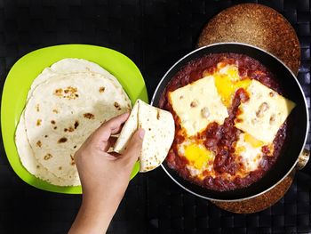 Cropped image of woman holding chapatti over food in bowl