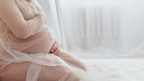 A happy pregnant woman holds her hands stomach sitting on a bed