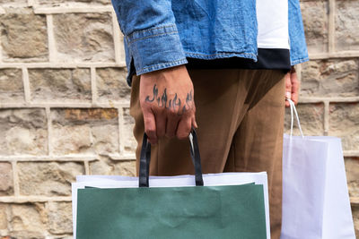 Crop unrecognizable man in trendy apparel with eco friendly bag standing on pavement near rough wall