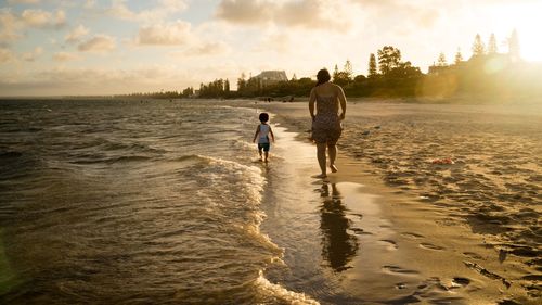 Rear view of father and son walking on sea shore against sky