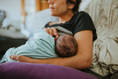 Midsection of woman breastfeeding baby on bed